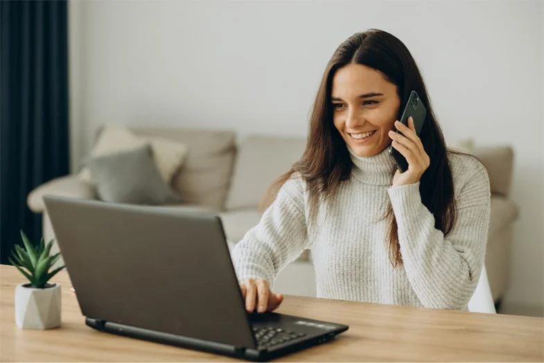 Mujer trabajando desde casa, sentada a una mesa con laptop y teléfono, reflejando el teletrabajo en España
