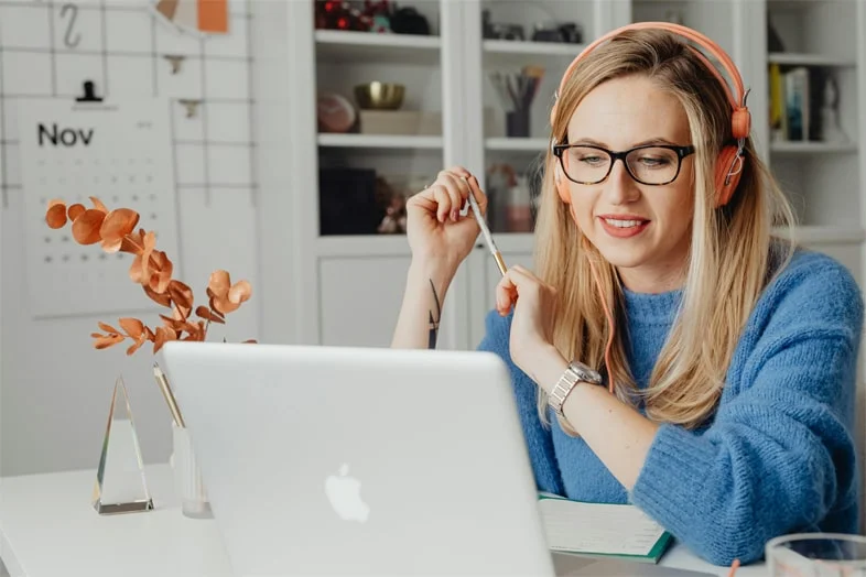 Mujer usando auriculares y gafas, concentrada en su portátil en un entorno de teletrabajo en España