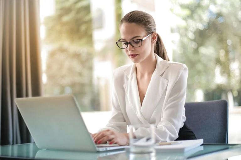 Mujer con gafas trabajando en su portátil, representando el teletrabajo en un entorno profesional y moderno